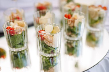 Şeffaf bardaklarda çoklu porsiyon salata. Açık hava yemekleri ya da etkinlik yemekleri için yansıtıcı bir yüzeye yerleştirilmiş..