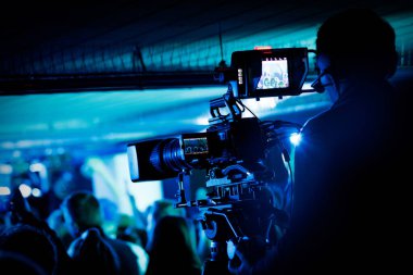 Mavi ışıkta canlı konser sırasında kameraman profesyonel kamera kullanırken yakın görüntüsü.