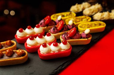 Kek çeşitleri ve kremalı turtalar ve siyah bir tabakta böğürtlen.