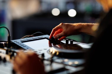 Yumuşak ışık altında canlı performans sırasında bir ses karıştırma konsolunun düğmelerini ayarlayan bir DJ 'in eli.