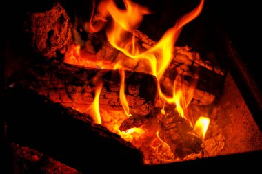 Parlak turuncu alevlerle yanan odunların ve açık havada parlayan közlerin yakın çekimi..