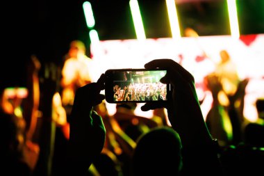 Kaldırılmış eller ve akıllı telefonların silueti yeşil ışıkta müzik performansını yakalıyor.