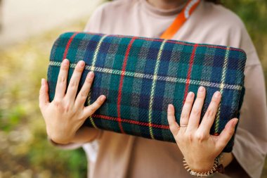 Piknik sırasında yeşil, mavi ve kırmızı desenli kareli battaniyeyi tutan ellerin yakın çekimi.