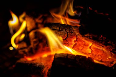 Turuncu alevlerle yanan odunların ve karanlıkta parlayan közlerin detaylı görüntüsü..