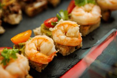 Ekmeğin üzerinde karides aperatifleri, salata sosu ve kiraz domatesleriyle servis edilir..