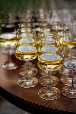 Yuvarlak ahşap bir masada sıralanmış beyaz şarapla dolu çoklu bardaklar, açık havada sığ bir tarla derinliğinde fotoğraflanmış..