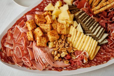 Büyük bir servis tabağına yerleştirilmiş dilimlenmiş et, peynir, kızarmış ekmek ve fıstık..