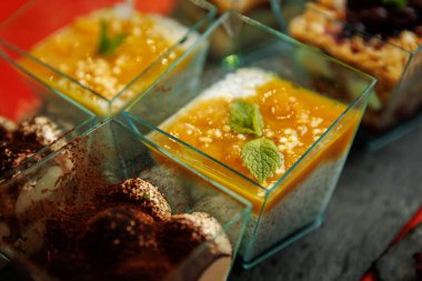 Parlak mango püresi ve taze nane yapraklarıyla kaplı kremalı tatlı dolu cam bardakların yakın çekimi..