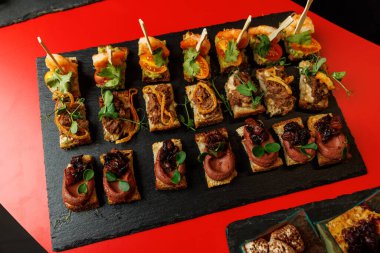 Kırmızı arka planda servis edilen karides, et ve sebzeli küçük aperatifler..