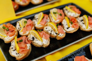 Küçük kanepeler füme somon, limon dilimleri ve krem peynirle servis edilir..