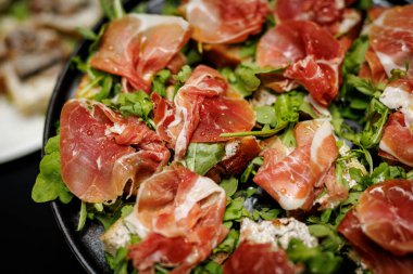 Taze roka ve siyah tabakta servis edilen ince jambonlu ekmek dilimleri..