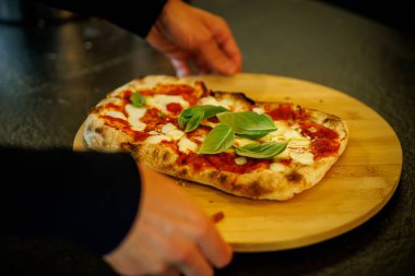 Eritilmiş mozzarella, domates sosu ve ahşap tahtada servis edilen taze fesleğenli sıcak margherita pizzası..