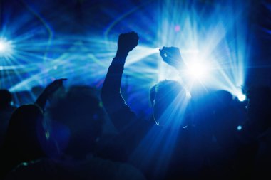 Canlı müzik konseri sırasında güçlü mavi lazer ışınları altında el kaldıran ve dans eden bir grup siluet..