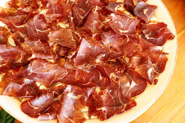 İnce dilimlenmiş jambon, aperatif ya da tapas olarak servis edilmeye hazır beyaz bir tabakta..