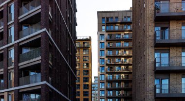 Kentsel bölgede tuğla ve cam cepheli ve sayısız balkonlu yüksek modern konut manzarası.