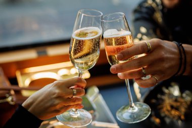 Kutlama sırasında şampanya bardaklarını tokuşturan iki kişi, sıcak ışık yansımalarıyla yakın çekim görüntüsü..