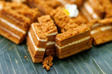 Geleneksel katmanlı ballı kek parçaları muz yaprağının üzerinde görünür krema dolgu ve kırıntıları ile servis edilir..