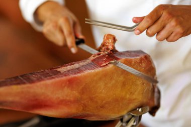 Mutfak ortamında uzun bir bıçak ve hassasiyetle iyileşmiş jambon bacağını kesen bir şefin yakın çekimi..