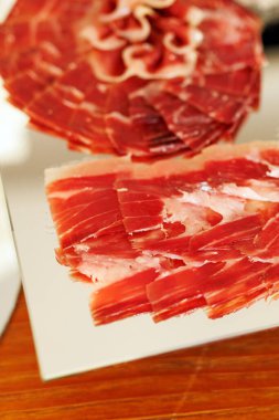 İnce dilimlenmiş jambon yakın plan. Ilık ışık altında yansıtıcı servis tabağına yerleştirilmiş..