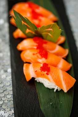 Yeşil yapraklı kırmızı balık yumurtası ile taze somon nigiri suşisinin dikey yakın çekimi..