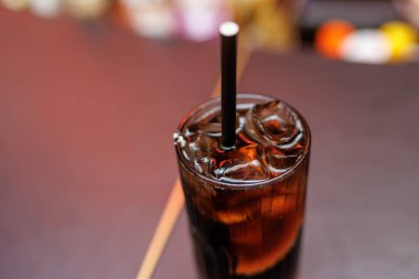 Buzlu soğuk, ferahlatıcı bir kola ve bulanık arka planda siyah bir pipet..