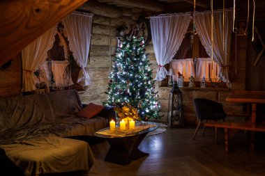 İç kısımları dekore edilmiş Noel ağacı, parlayan mumlar, ahşap duvarlar ve kırsal tatil atmosferiyle dolu..