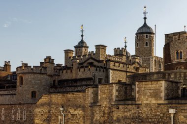 Ortaçağ kuleleri ve sıcak akşam ışığında dokulu taş duvarlarla Londra Kulesi 'nin detaylı görüntüsü. Tarihsel kale mimarisi açık bir gökyüzüne karşı duruyor.
