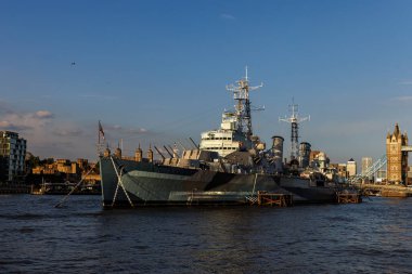 HMS Belfast 'ın tam görüntüsü Thames Nehri' nde Tower Bridge ve Londra Kulesi 'nin arka planında. Tarihi savaş gemisi ve akşam ışığı altında dönüm noktaları.