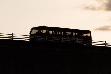 Bir Londra otobüsü gün batımında köprüden geçerken gökyüzüne karşı gölgelenir..