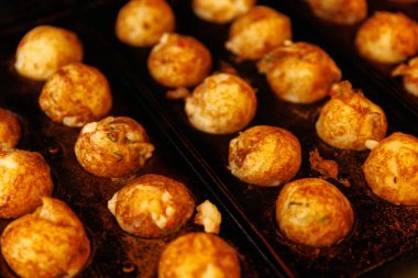 Demir ızgarada pişen altın takoyaki sıraları. Yakın çekim desen, renk ve sokak yemekleri atmosferini vurguluyor..