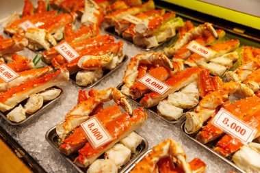 Kırmızı yengeç bacakları, deniz ürünleri reyonunda görünür fiyat etiketleriyle buzun üzerinde düzenlenir. Parlak ışıklandırma tazeliği ve rengi vurgular.