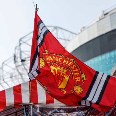 Manchester, İngiltere - 17.08.2025: Red Manchester United bayrağı açık bir günde Old Trafford Stadyumu yakınlarında dalgalanıyor. Görüntü, arka planda kulüp renklerini ve stadyum mimarisini gösteriyor..