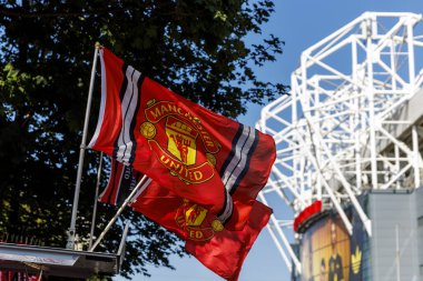 Manchester, İngiltere - 17.08.2025: Açık mavi gökyüzü altında bir stadyum binasının önünde dalgalanan parlak kırmızı bayraklar.