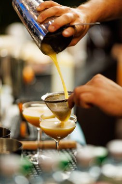 Bir barmen bir coupe bardağına yeni sallanmış bir kokteyl döker ve süzer. Kapanış sahnesi miksoloji, zanaat içkileri ve bar servisi..
