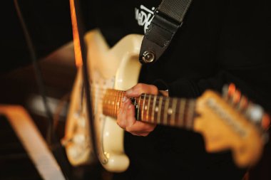 Kapalı alan provası sırasında elektro gitar çalan bir müzisyenin ellerinin yakın çekimi. Enstrüman tellerine ve anlamlı performansa odaklan.