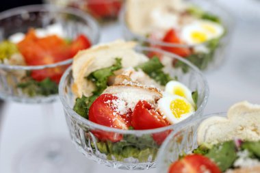 Zarif cam kaselerde servis edilen tavuk, domates ve yumurtalarla salata porsiyonlarını kapatın..