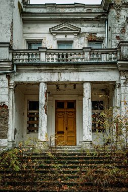 Çürüyen boyalar, çatlak duvarlar ve kapalı sarı kapılar olan bir bina. Yapı yıpranmış ve terk edilmiş görünüyor..
