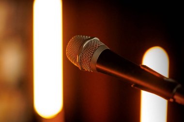 Sıcak sahne ışıklarıyla aydınlatılan bir mikrofon, seyirciye doğru dönük. Sığ alan derinliği bir konser havası ekliyor..