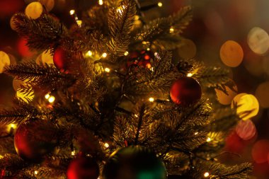 Kırmızı küreler ve parlak peri ışıklarıyla süslenmiş gür bir çam ağacının yakın görüntüsü.