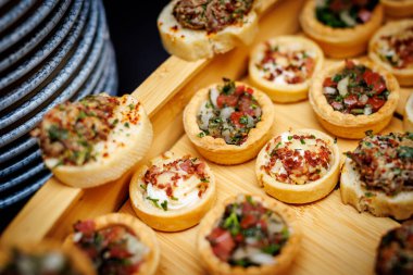 Tahta tepside çeşitli lezzetli malzemelerle küçük tart ve ısırık büyüklüğünde atıştırmalıklar..