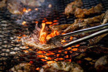 Görünür duman ve metal maşalarla yanan et parçalarının yakın çekimi..