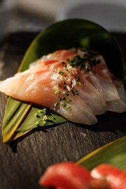 Bitkilerle tatlandırılmış ve yaprağın üzerinde servis edilen ince çiğ beyaz balık dilimleri..