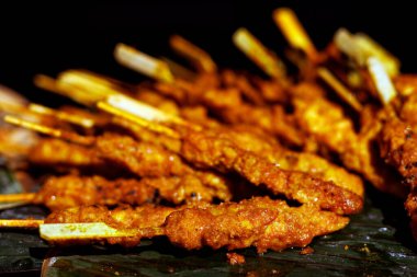 Bir yığın baharatlı ızgara tavuk şişi sıcak ışıkta gösteriliyor, altın rengi ve dokuları vurgulanıyor. Görüntü lezzetli sokak yemekleri ızgarasını vurguluyor..