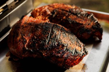 Izgaranın yanındaki metal tepside duran kömürleşmiş kabuklu iki büyük et parçasının yakın çekimi..