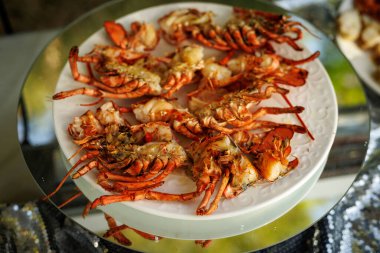 Açık hava yemeği sırasında beyaz bir tabakta birden fazla ızgara ıstakoz yarısı. Izgara kabuklu deniz ürünleri ve zengin dokulu deniz ürünleri..