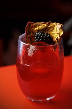 Buzlu kırmızı bir kokteyl altın süslemeli ve üstünde böğürtlen ile servis edilir..