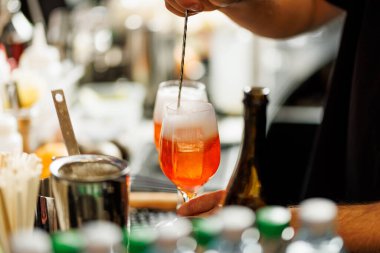 Bir barmen, barın üstünde portakal renkli bir kokteyl karıştırır..