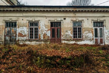 Boya soyan, tuğla döken ve kırık camları olan yıpranmış bir yapı bakımsız, fazla gelişmiş bir bölgede duruyor. Resim çürüme ve uzun süreli terk edilme belirtilerini gösteriyor..
