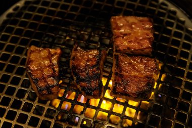 Parlayan sarı közlerin üzerinde metal bir tel askıda kurutulan yüksek kaliteli biftekler. Izgaradaki yağlar yanmış bir kabuk oluşturuyor..