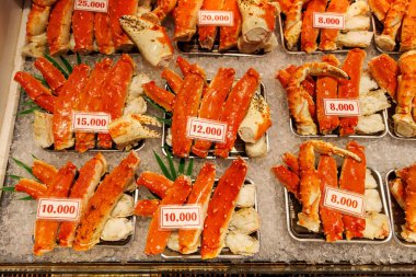 Yen fiyat etiketleriyle ezilmiş buz üzerinde soğutulmuş kırmızı yengeç bacakları ve pençeleri sergilenir.
